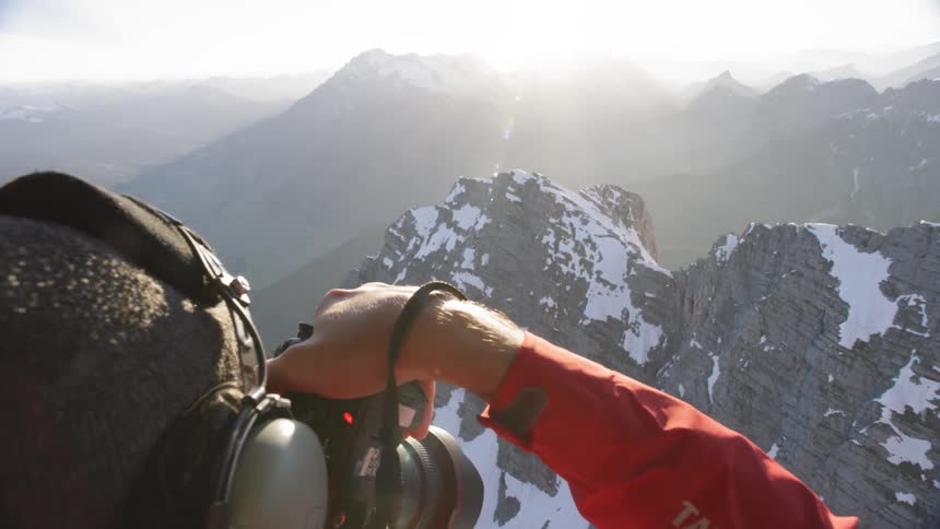 A photographer takes pictures of snowy mountain peaks while flying in a helicopter