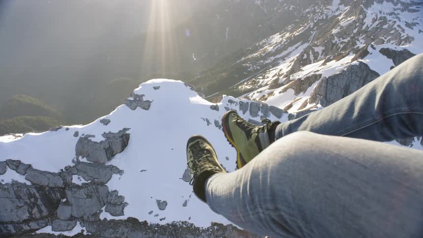 A persons legs hanging out of a helicopter over mountains