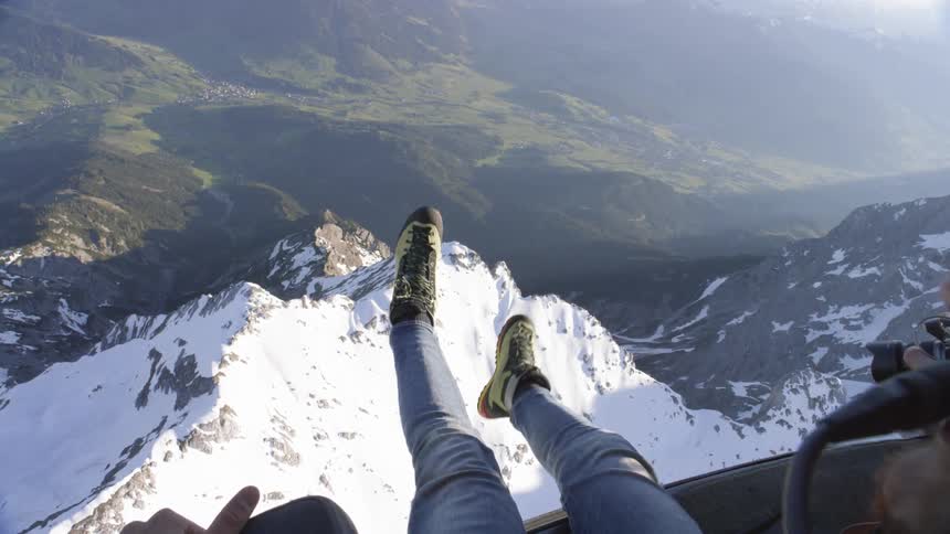 A photographer hangs his feet from the side of a helicopter flying over mountains