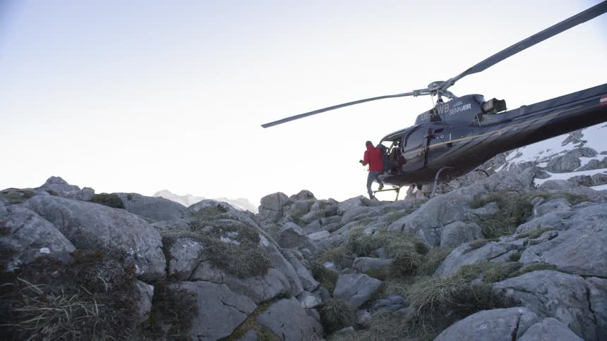 A man gets out of a helicopter that has landed on a rocky hill
