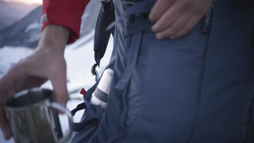 A person is grabbing a cup from a backpack
