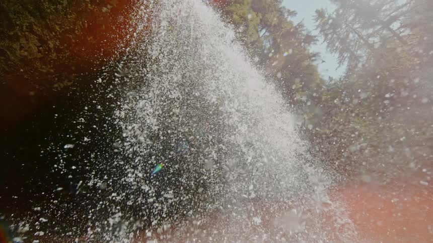 Water cascades directly downward from a waterfall and splashes vigorously below causing droplets and mist to fly in all directions