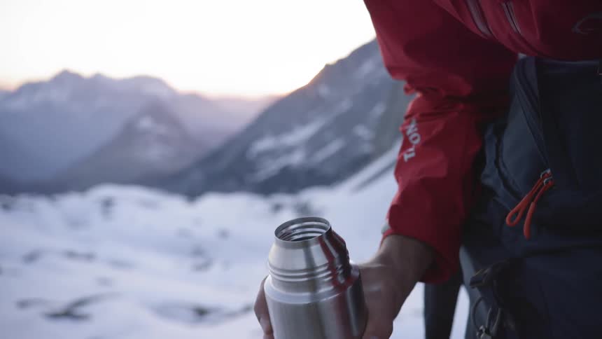 A person pours a drink from a thermos on the mountain
