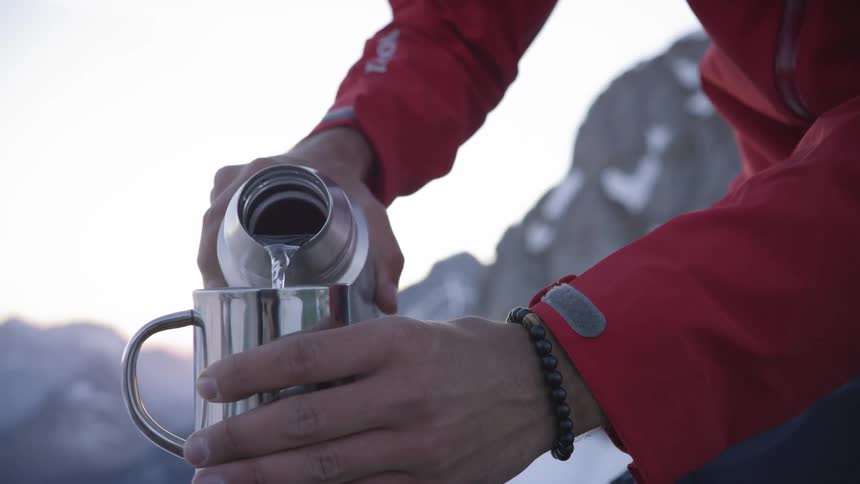 A white man pours water from a thermos into a metal cup
