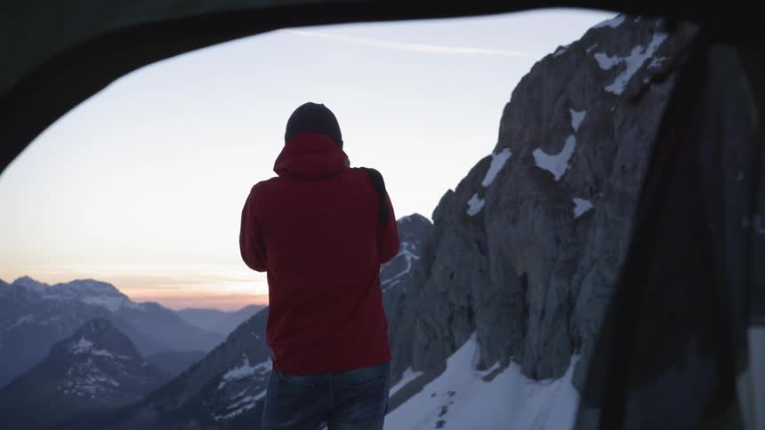 A man with a camera and a red hoodie taking a picture of a mountain