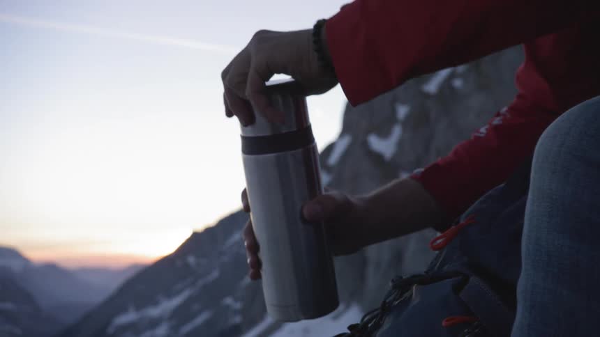 A person unscrews his thermos on the mountain