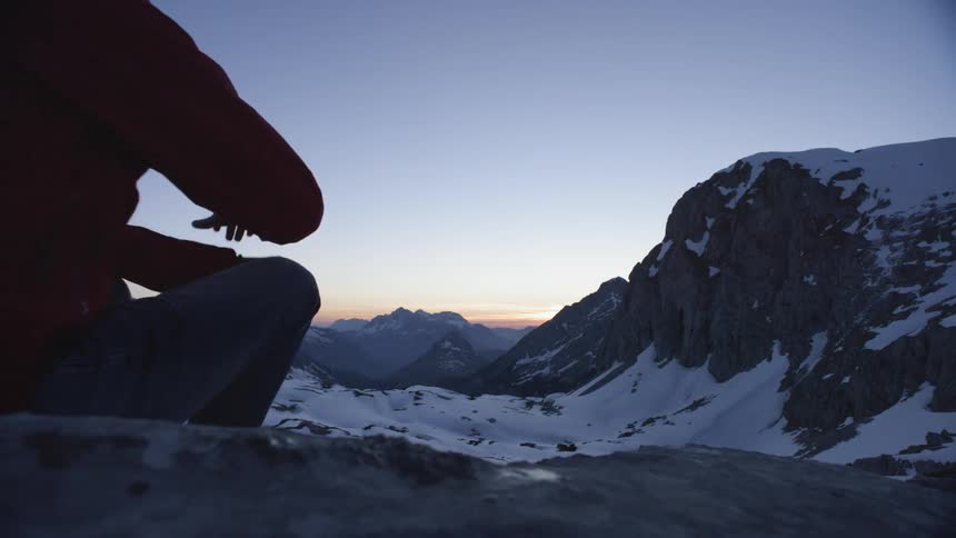 A man sits on the snow covered rocks near a mountain range