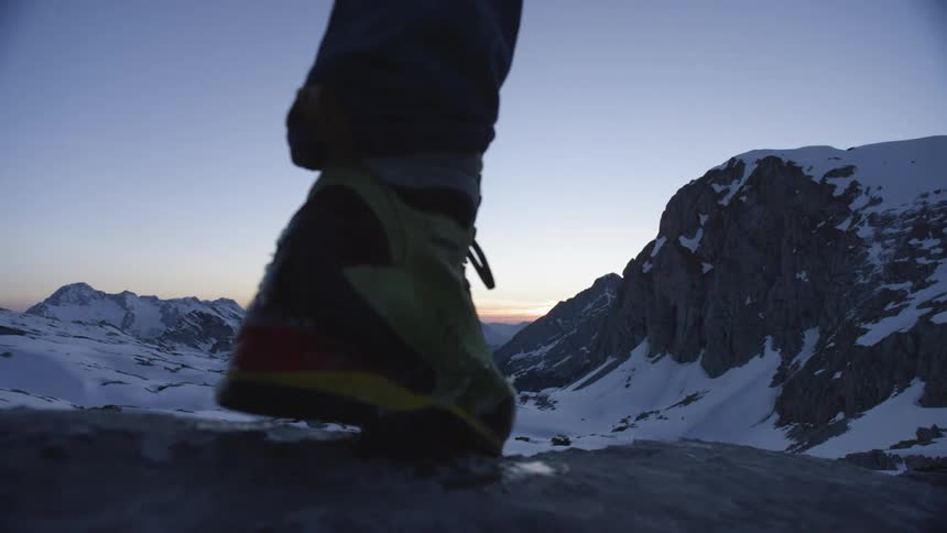 Person stands to look over sun setting past mountains