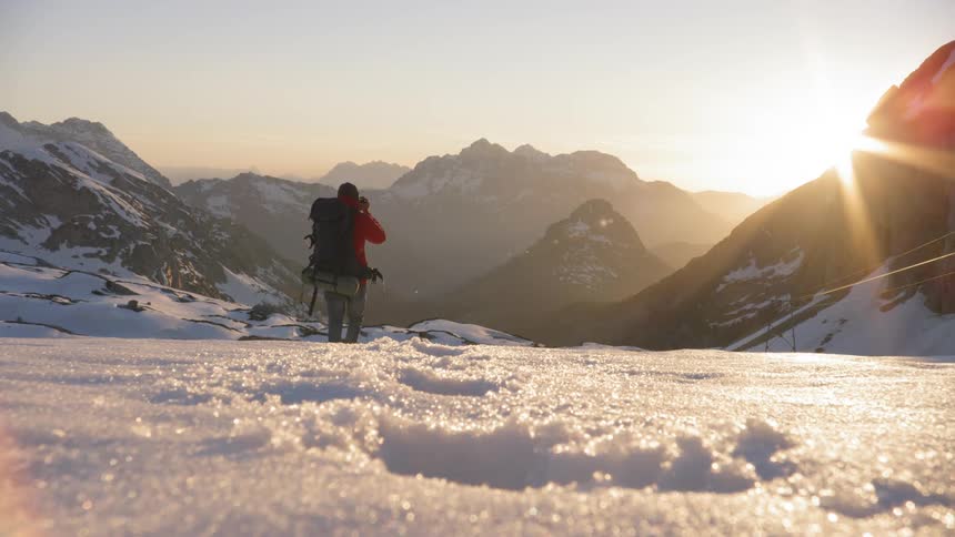 A hiker walking through snowy terrain in the mountains before taking a photo of the horizon