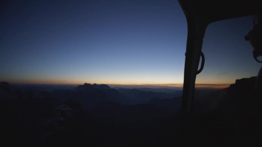 A helicopter flies over mountains at dusk
