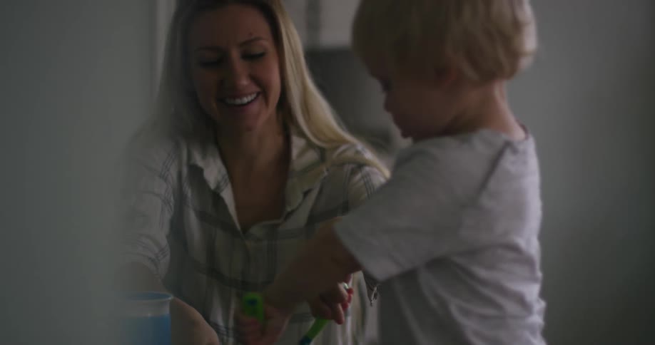 A woman helps her toddler use utensils on his food