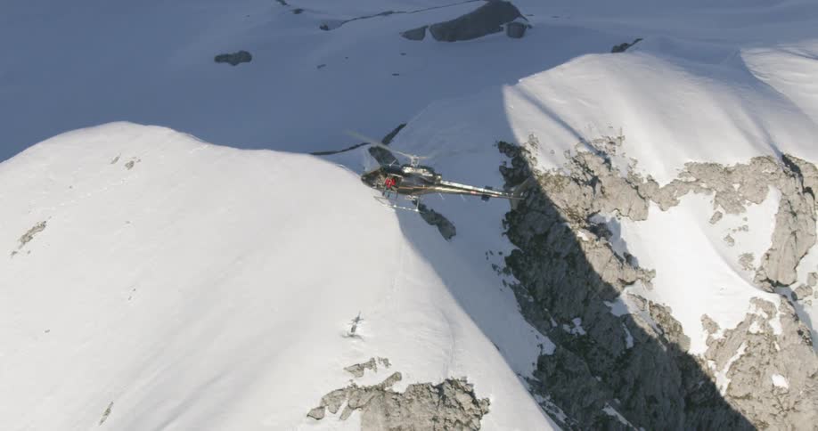 A helicopter spins stationary over a snow topped mountain