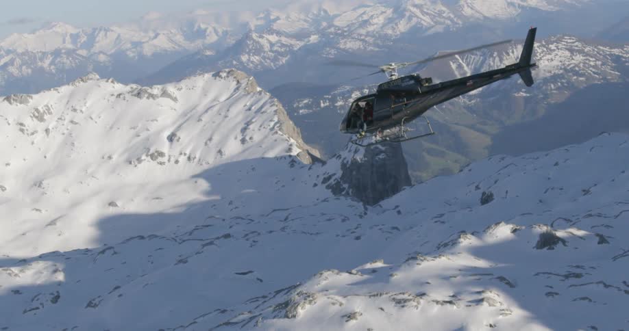 The helicopter is flying over the snow covered mountain