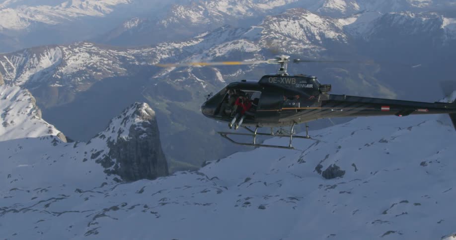 A helicopter hovers over the snow covered mountains