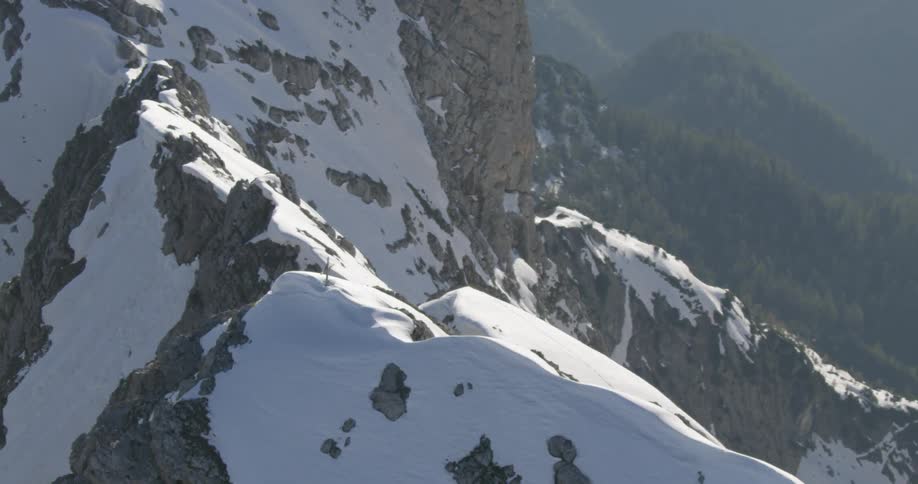 A cross stands on top of a snowy mountain peak