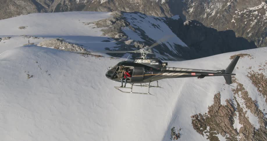 A helicopter flies over a snow covered mountain range