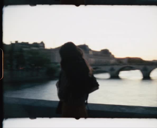 A woman walks a pedestrian bridge and stops to take something out of her purse