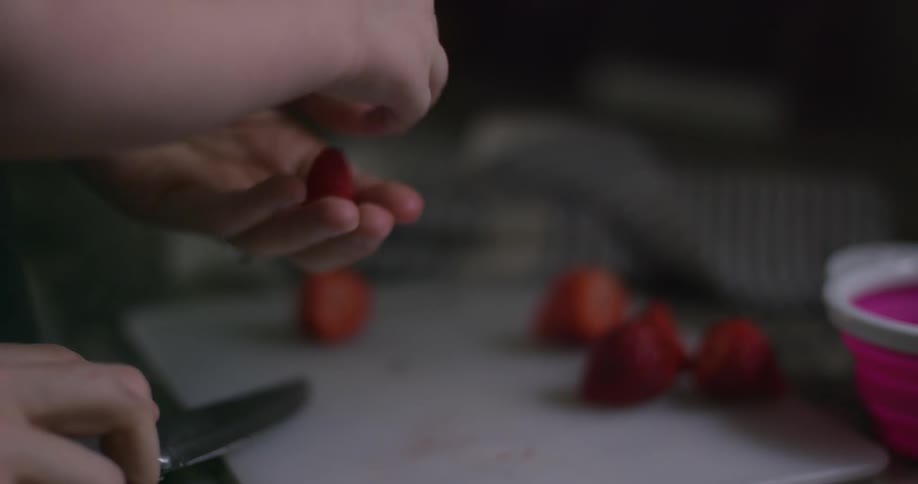 A man cuts up fruit and feeds it to a young child