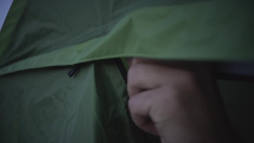 A man is closing the zipper of an opening to a green tent from the inside