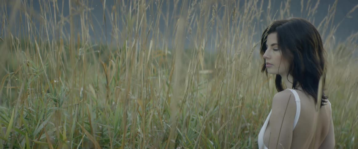 A woman walks through a field and poses