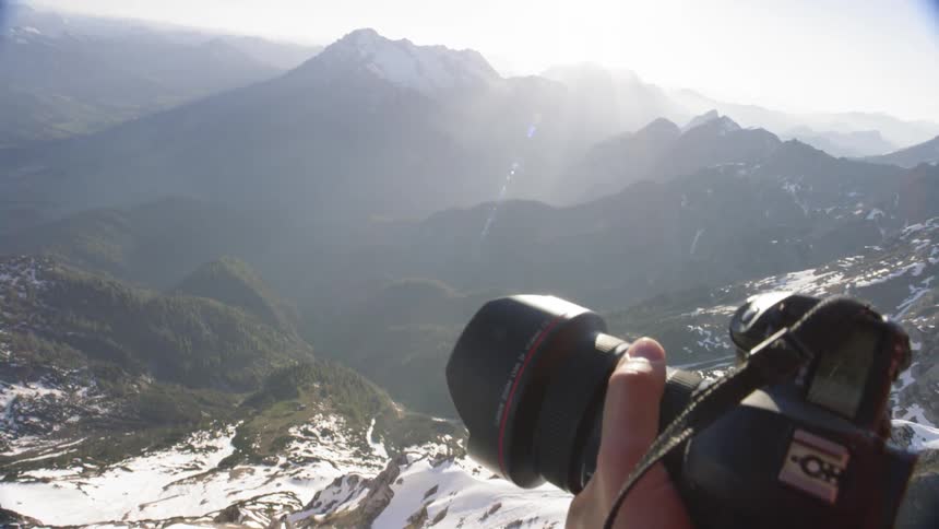 Man holds a camera as he sits outside of a flying helicopter