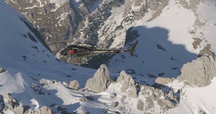 A helicopter flies above a snow covered mountain pass