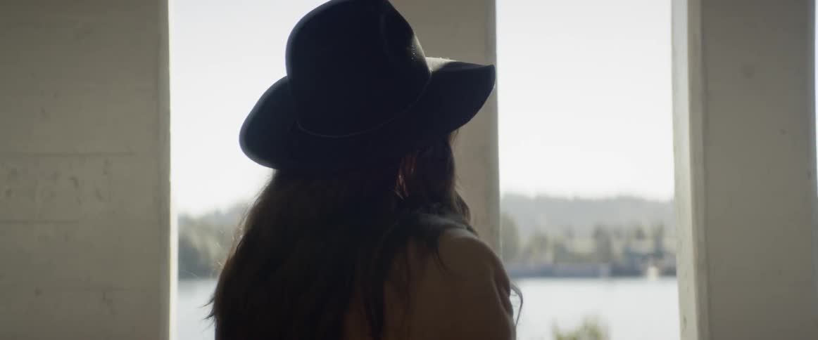Woman wearing wide hat takes a picture of distant city on a sunny day