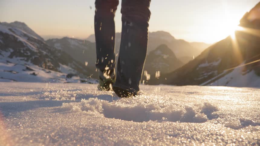 A man walks through ankle deep snow that is on the ground as he make his way towards a mountain range in front of him
