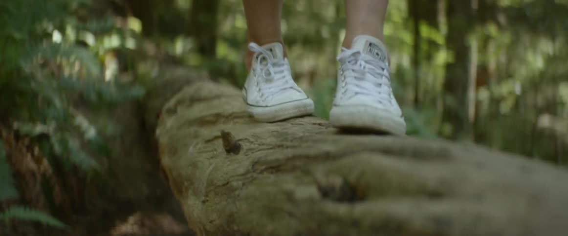 Close up of white tennis shoes walking across a log in the forest