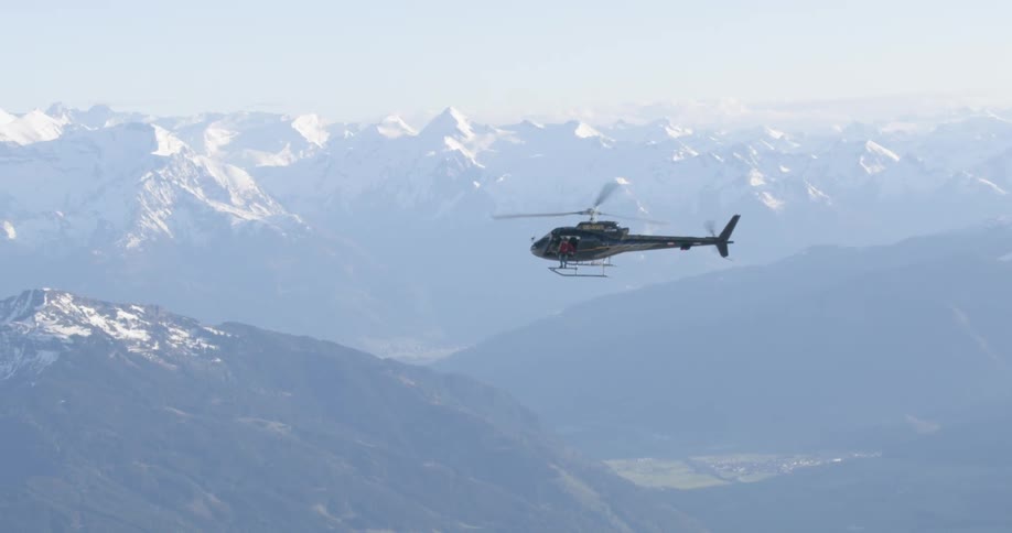 A helicopter flies over snow covered forests and hills