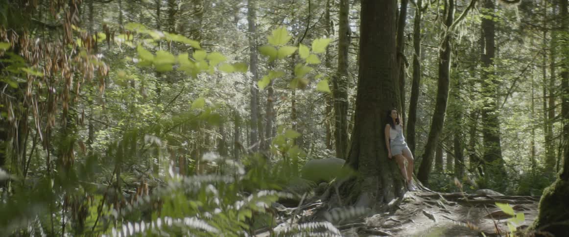 Woman leans against a tree in woods during daylight