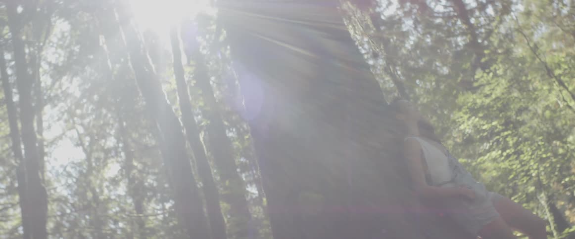 A woman standing in the forest leaned up against a large tree