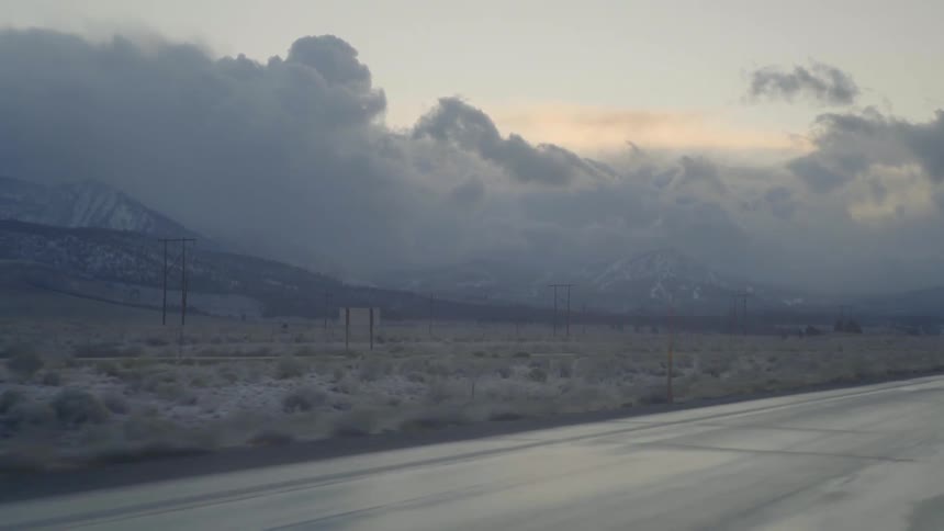 A truck drives down a road with dark clouds and mountains in the background