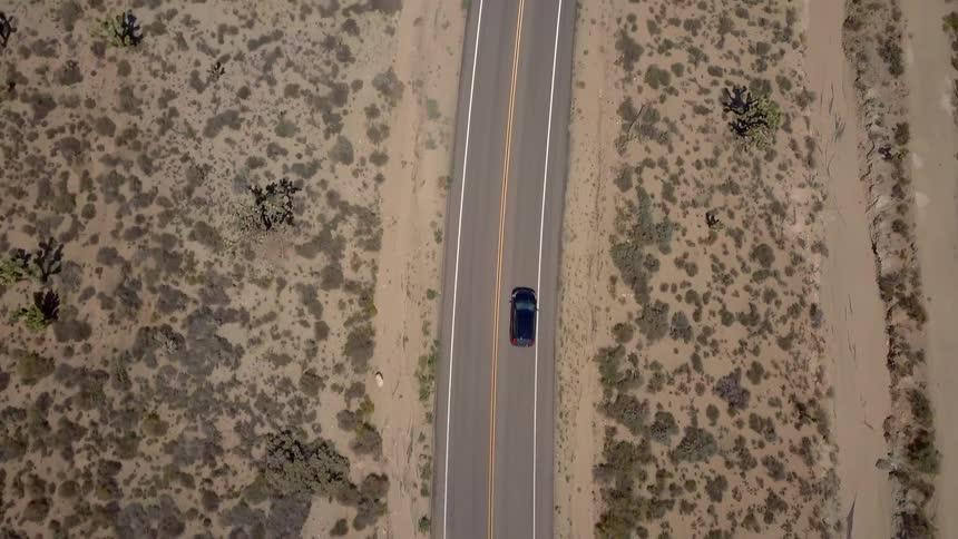 A black car speeds down a two lane road in the desert