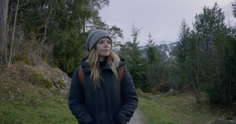 Woman wearing coat and wooly hat walks on the forest track in the woods on a cloudy day