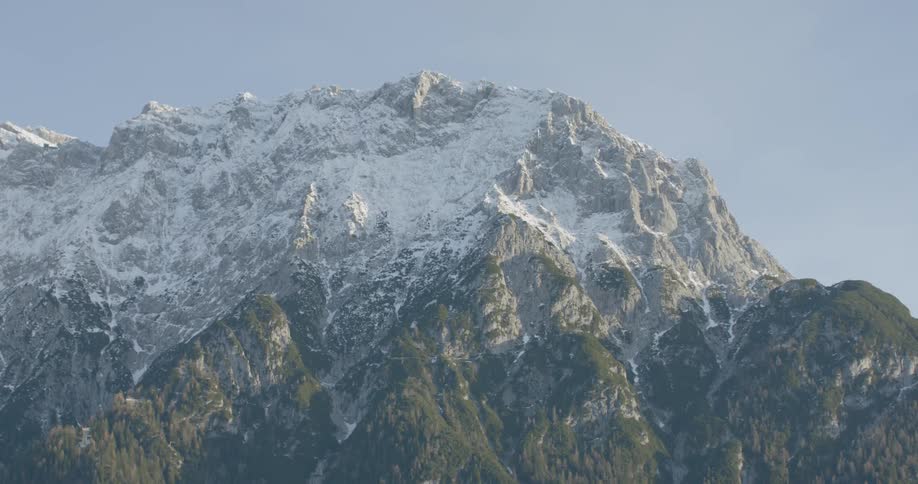 A tall mountain has snow on the peak but green vegetation growing on the bottom