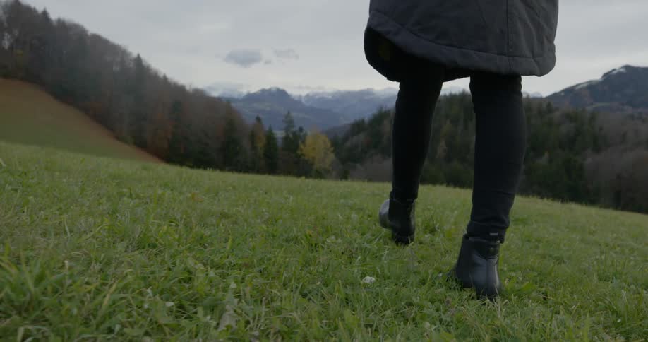 A woman walks through the grass near a forest