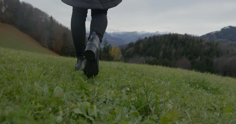 Person walks along grass covered field toward mountains on horizon