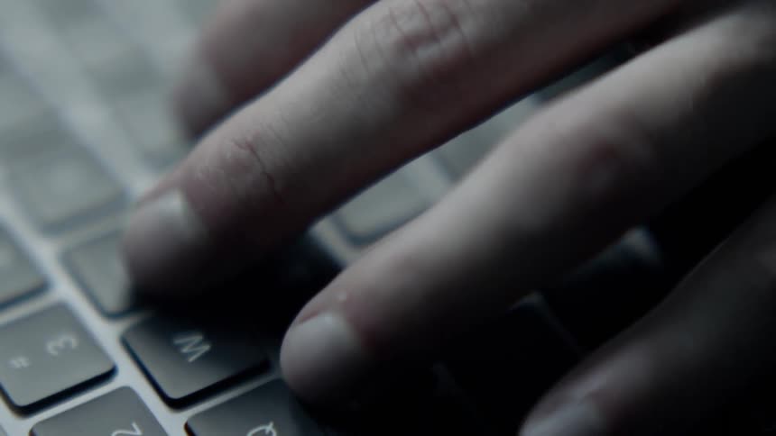 A white man types on a laptop keyboard