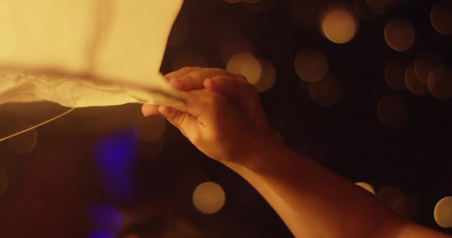 An adult holds child's hand and balloon before it lifts at night