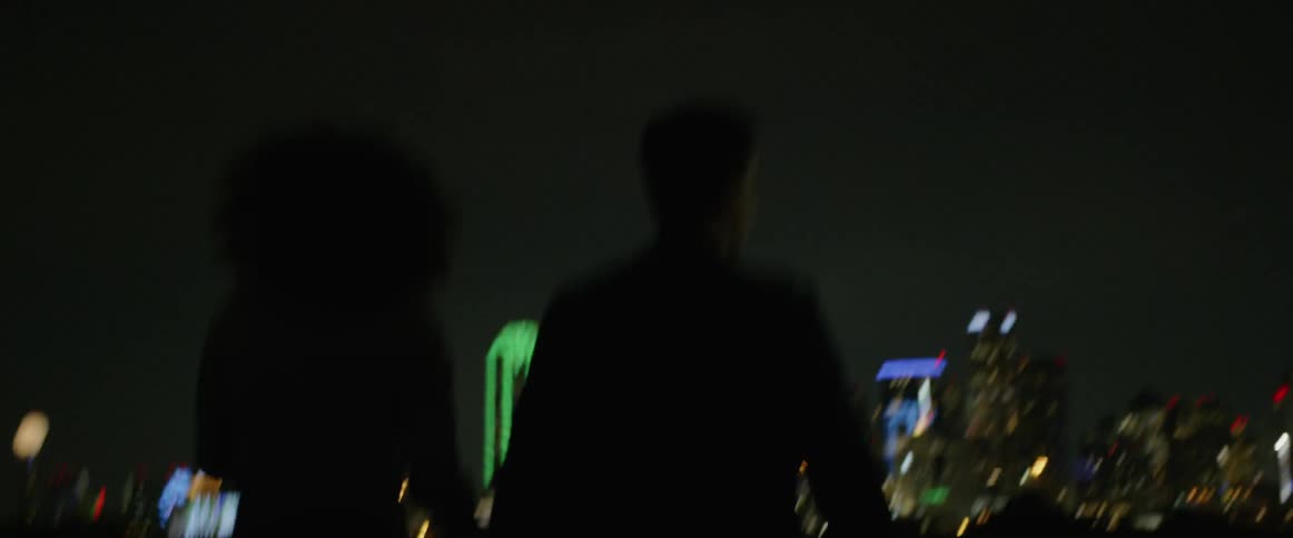 Couple walk hand in hand toward downtown city lights at night