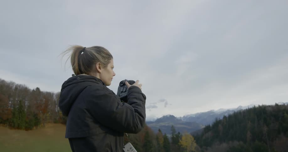 A white female is taking photographs of mountains and forest with a fairly large camera from an elevated position