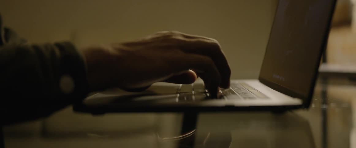 A man finishes typing something on a laptop on a glass table before closing it