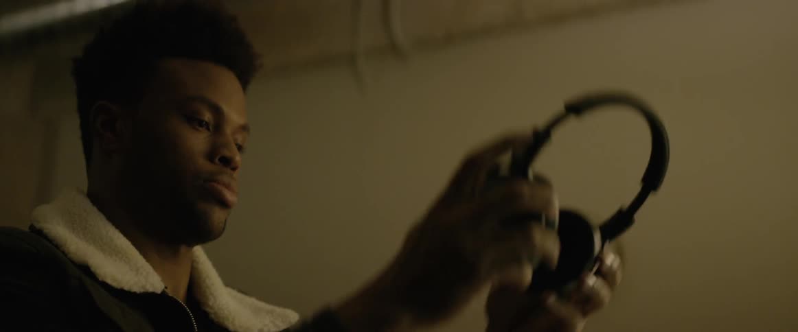Black man sitting wears headphones in a room at night