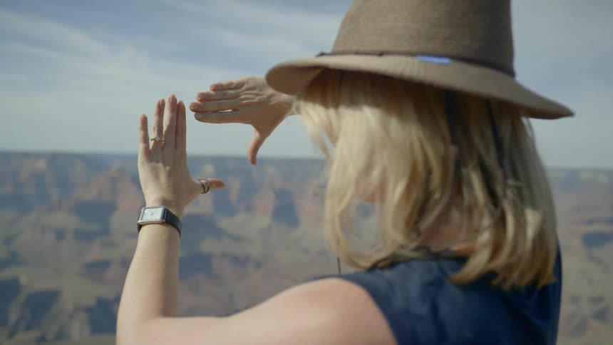Woman stands on edge of canyon and considers possible picture framing