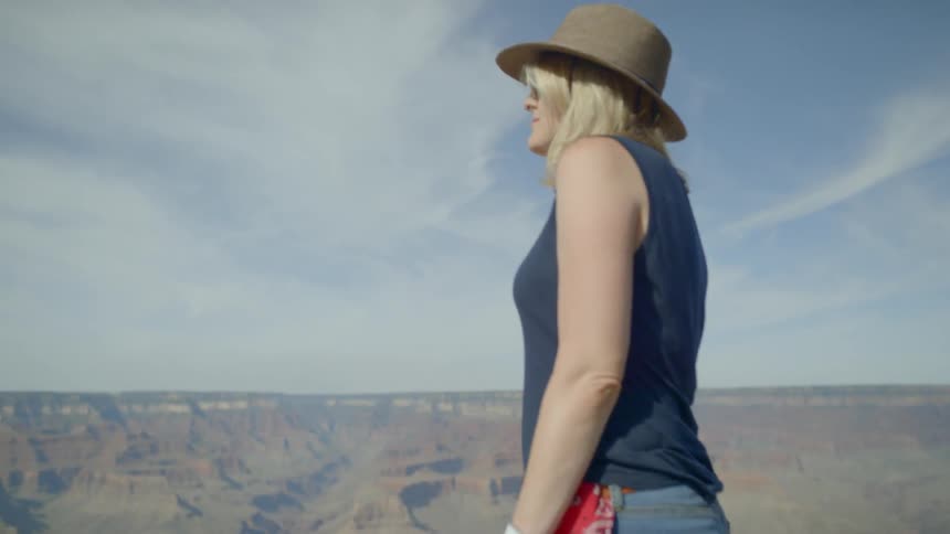 Woman walks along a rock and looks out at the mountains on a sunny day