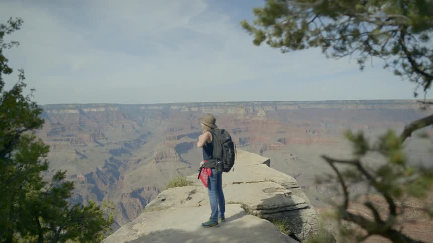 A woman walks along a cliff edge and takes her backpack off