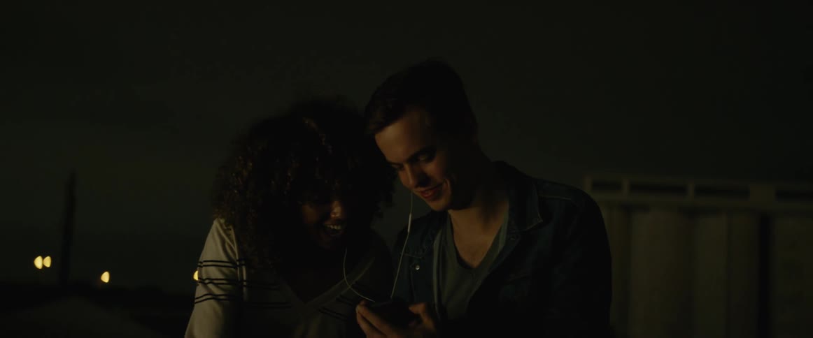 Man and woman sit outdoors at night sharing earphones