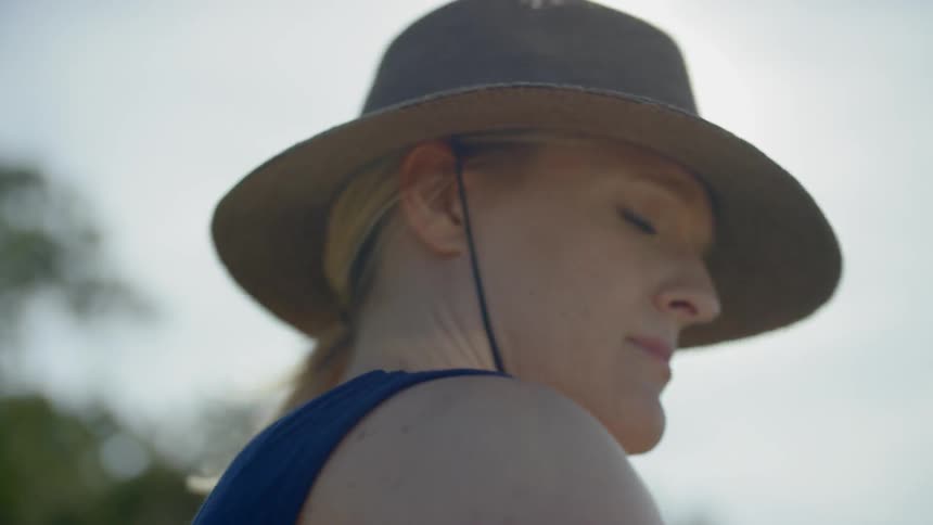 Blonde woman wearing wide hat looks around outside on a sunny day
