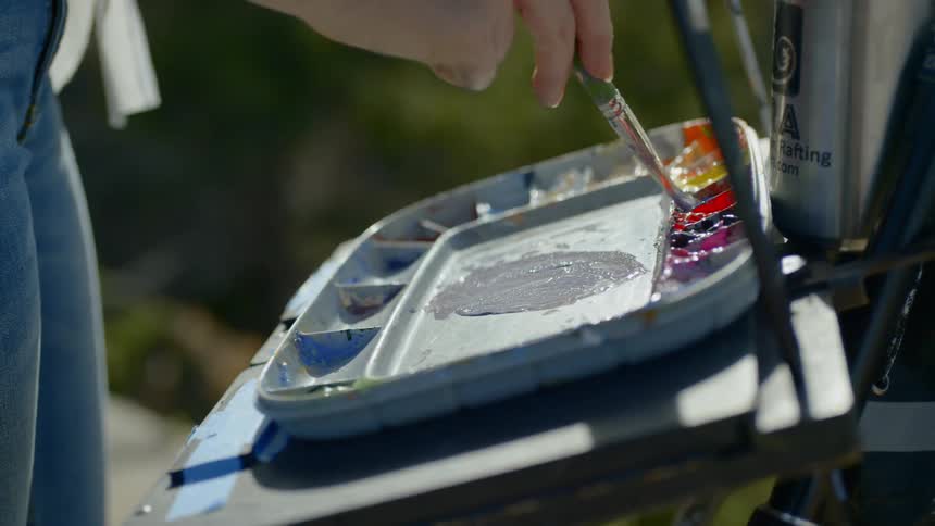 A woman standing outside with a paintbrush mixing paint